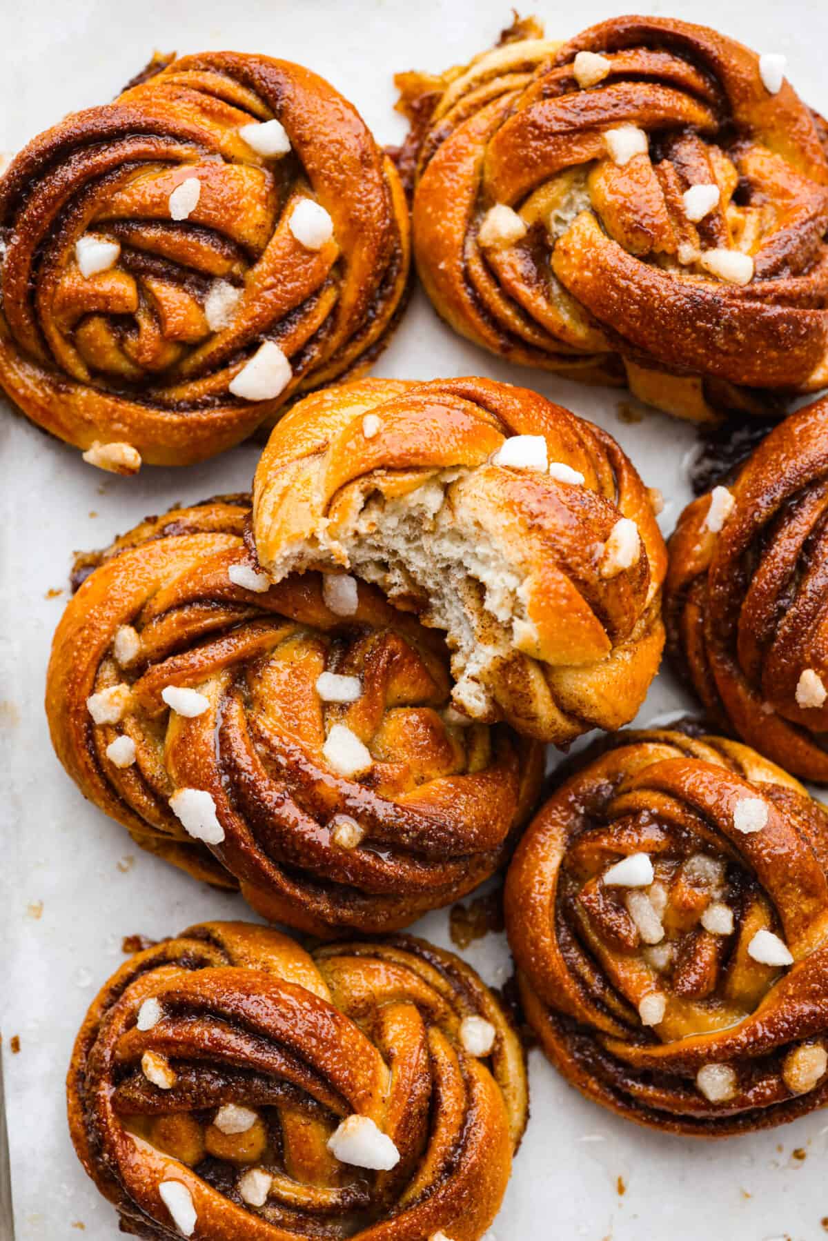 Closeup of kanelbullar buns topped with pearl sugar. One has been torn in half.