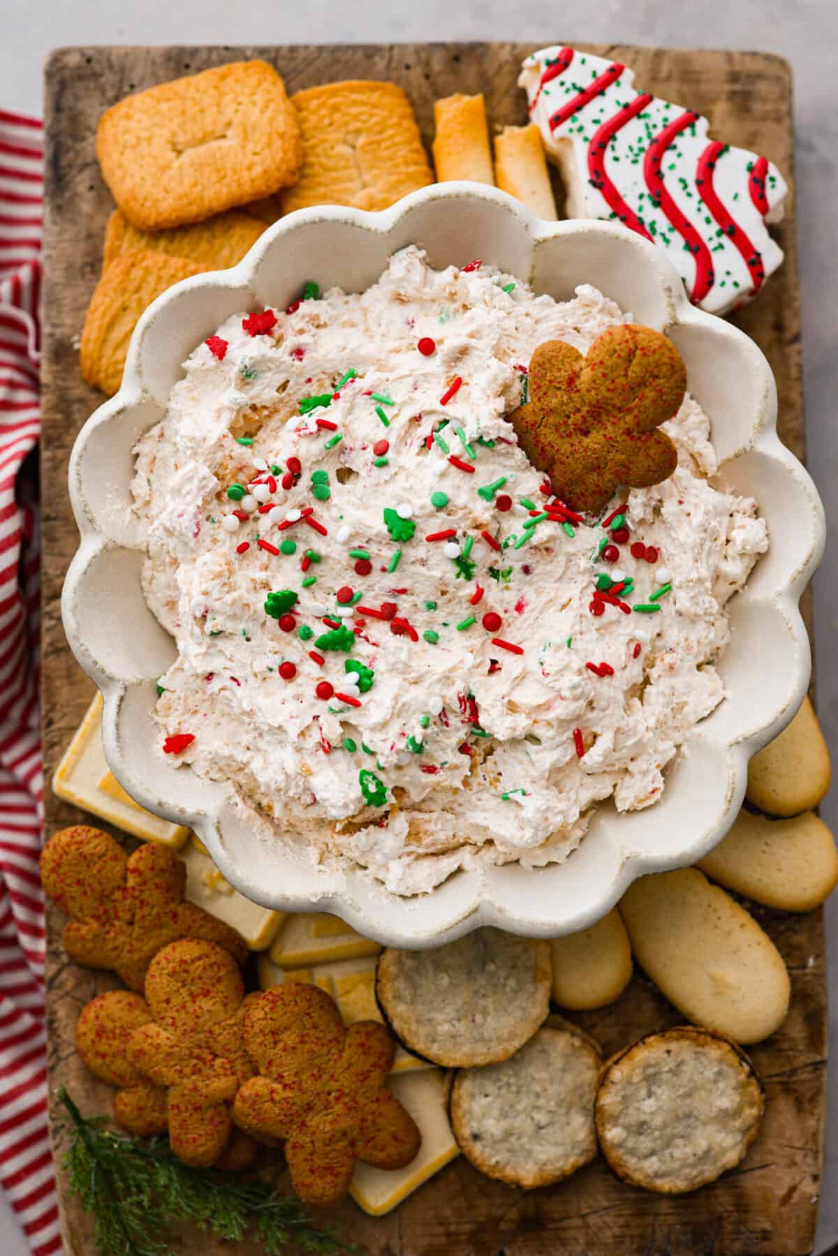 A bowl of Christmas tree dip surrounded by various cookies.