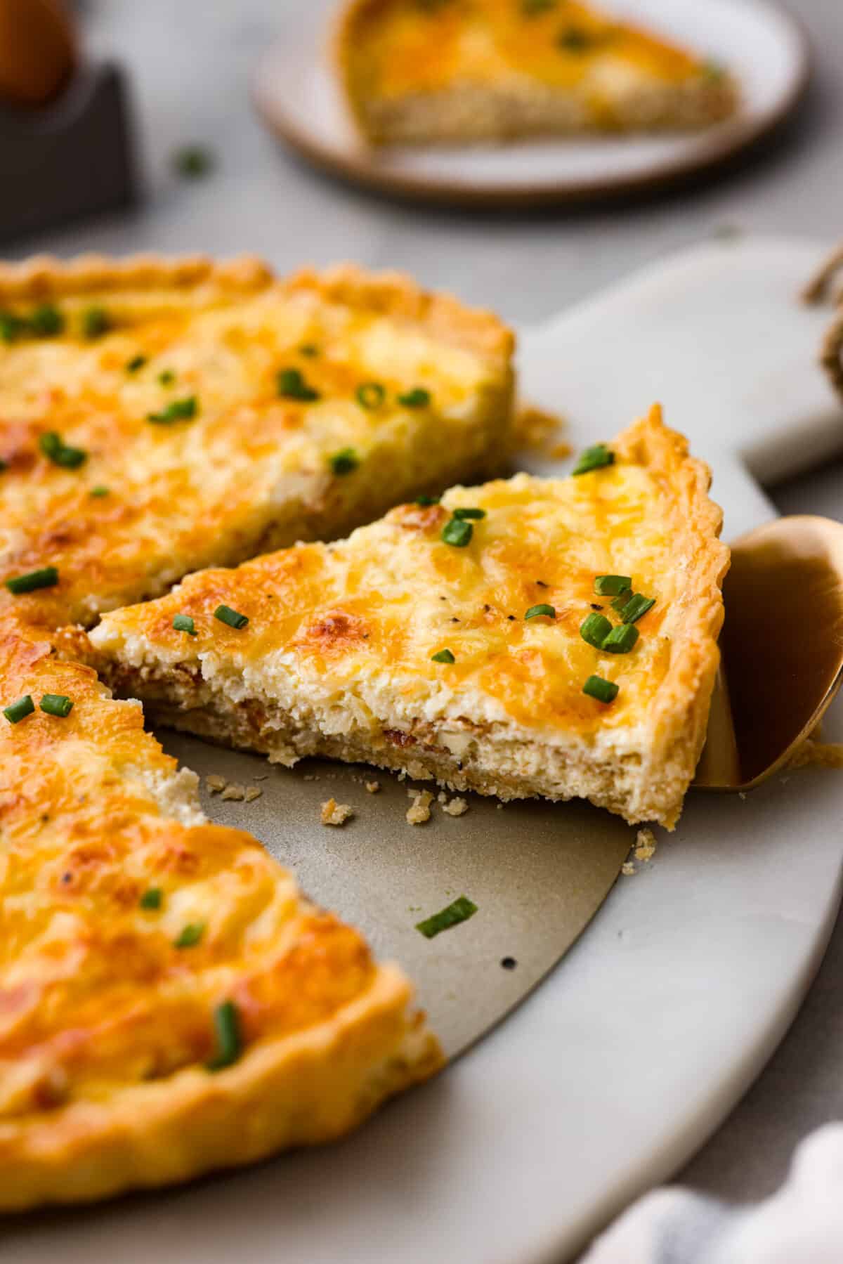 A slice of quiche being served with a metal spatula.