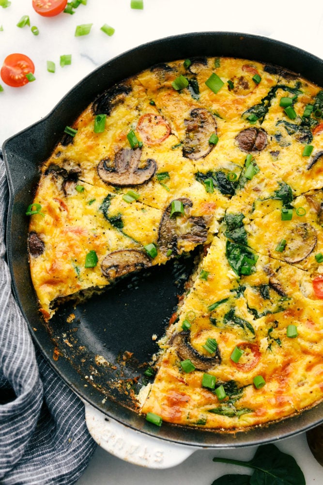 Breakfast frittata cooked on a skillet with a slice of frittata missing from it. 