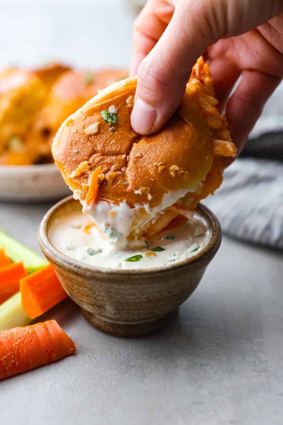 A buffalo chicken slider being dipped into ranch sauce. 