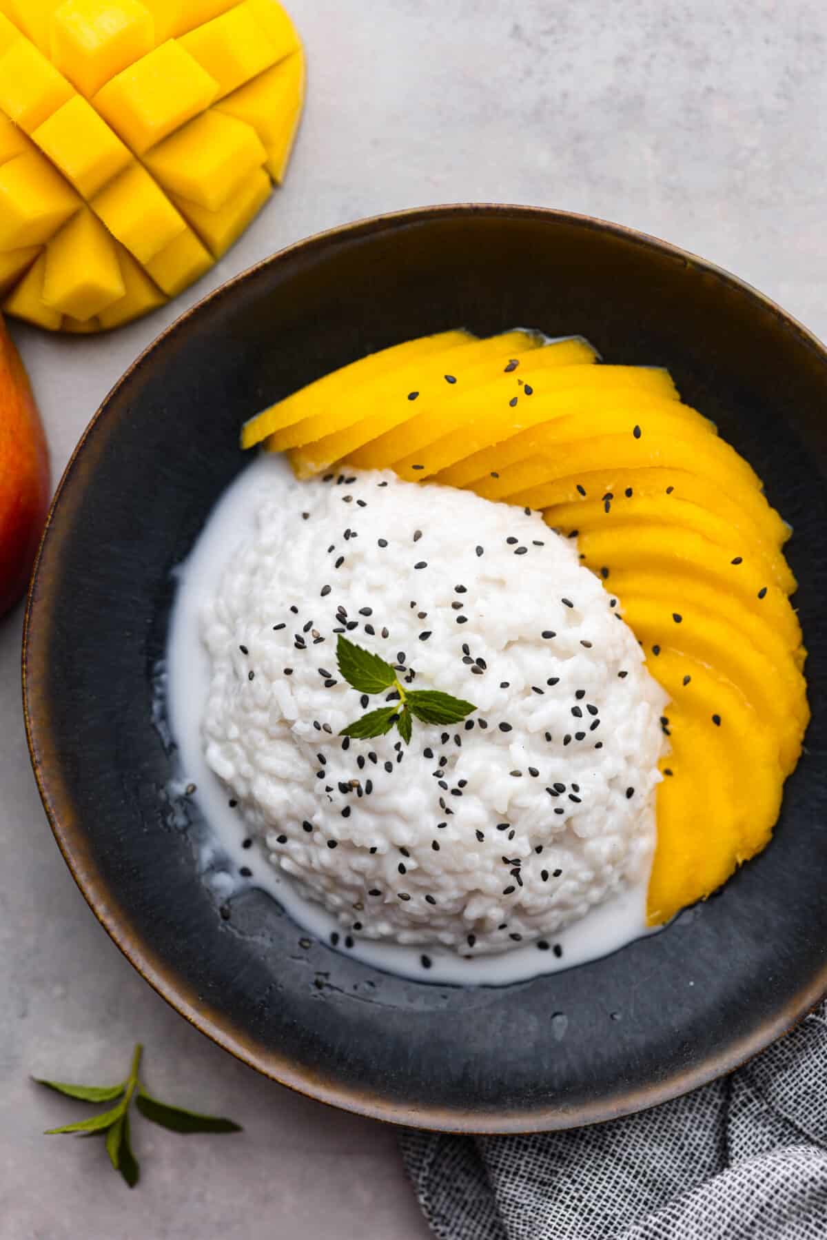 Top-down view of sticky rice served with coconut sauce and sliced mangoes.