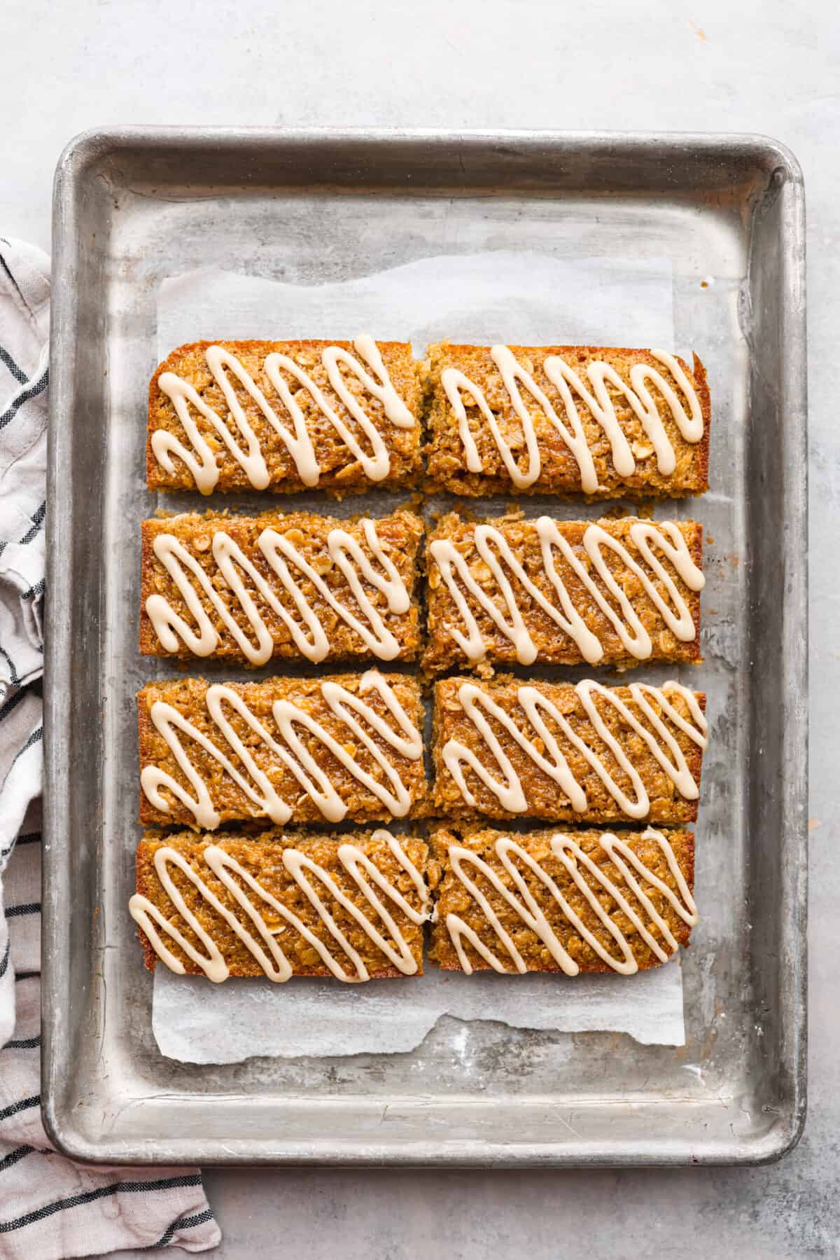 Cooked breakfast bars with a glaze that are on parchment paper on a baking sheet. 