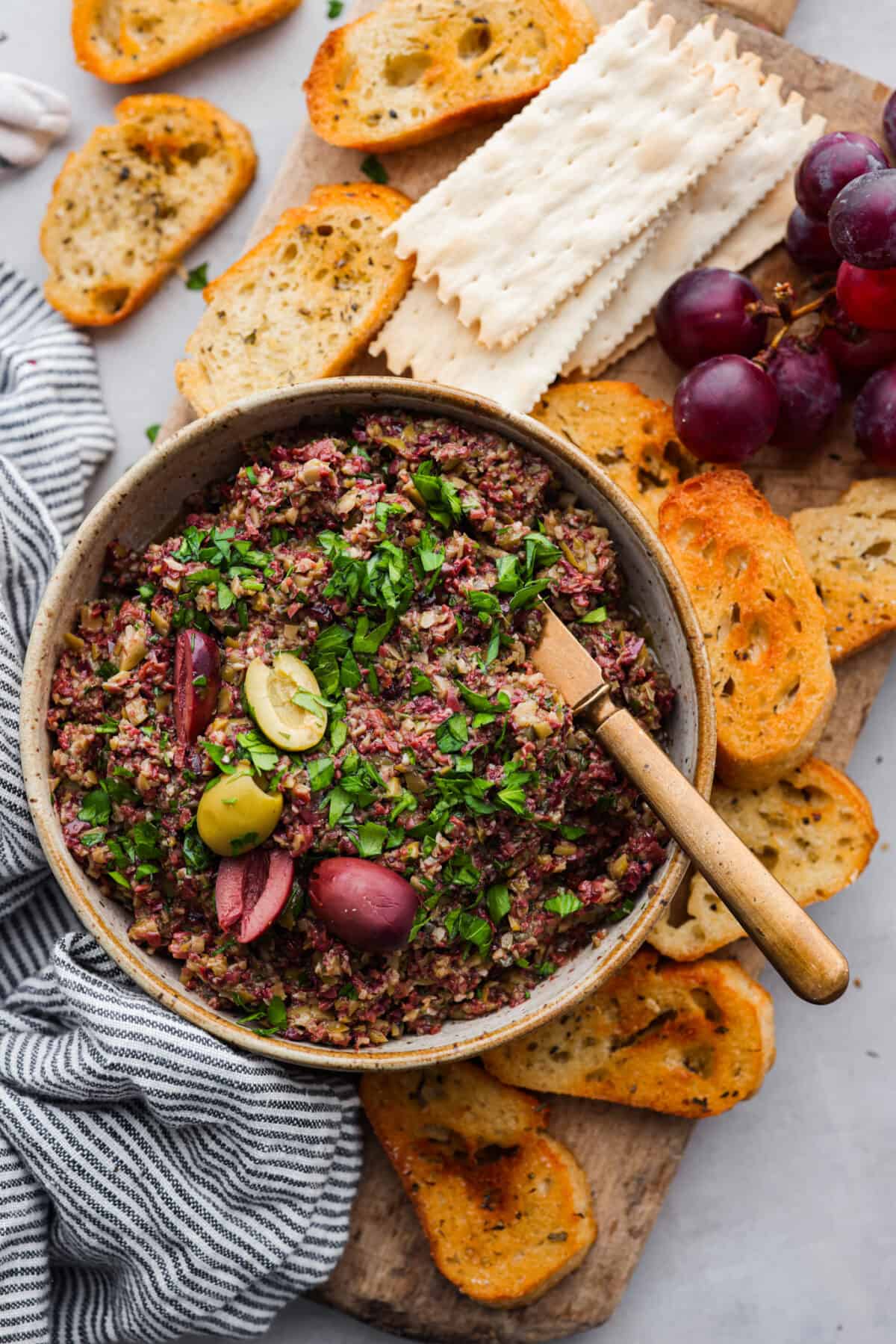 Top view of tapenade in a brown bowl served with crostini and crackers.