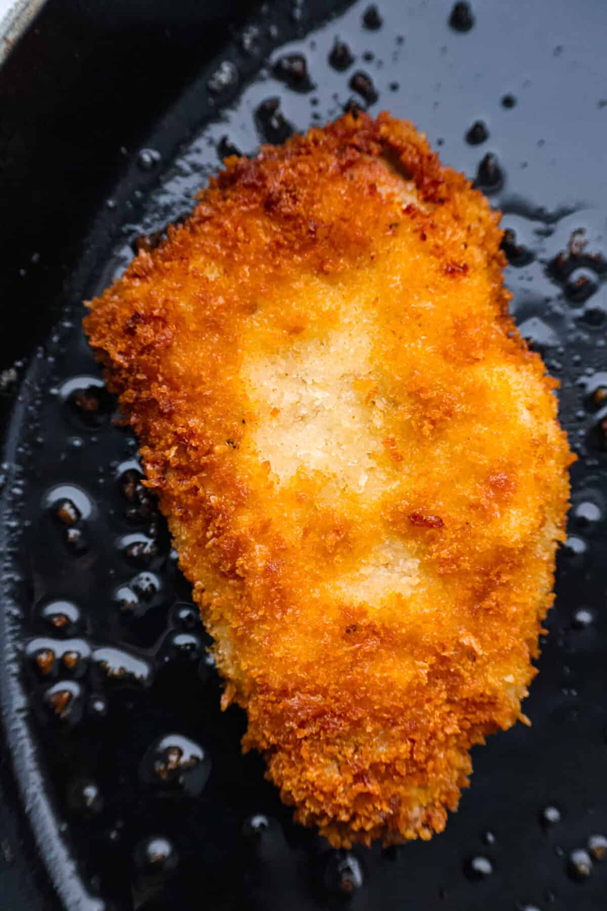 Closeup of a pork cutlet being fried in oil.