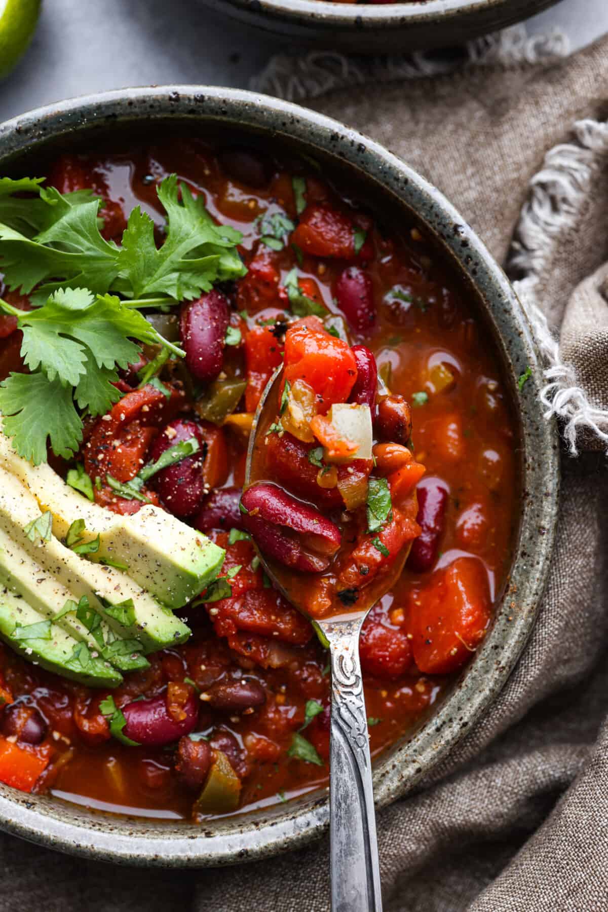 Close up of chili in a gray bowl topped with cilantro and avocado.