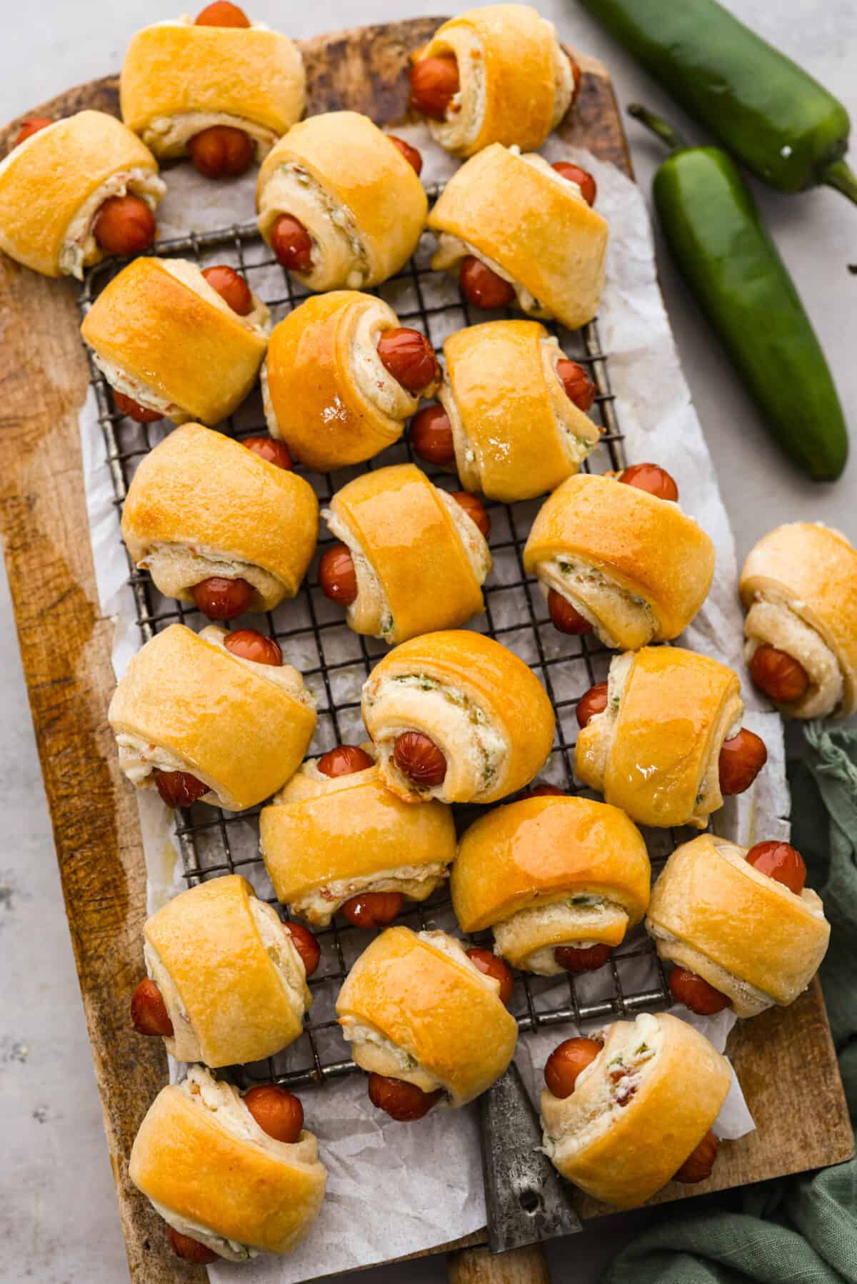 Top view of jalapeno popper pigs in a blanket on a wood board lined with a cooling rack.