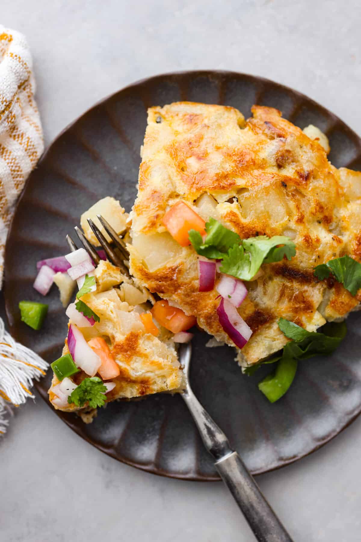 Close view of a slice or Spanish tortilla on a small plate with a fork. 