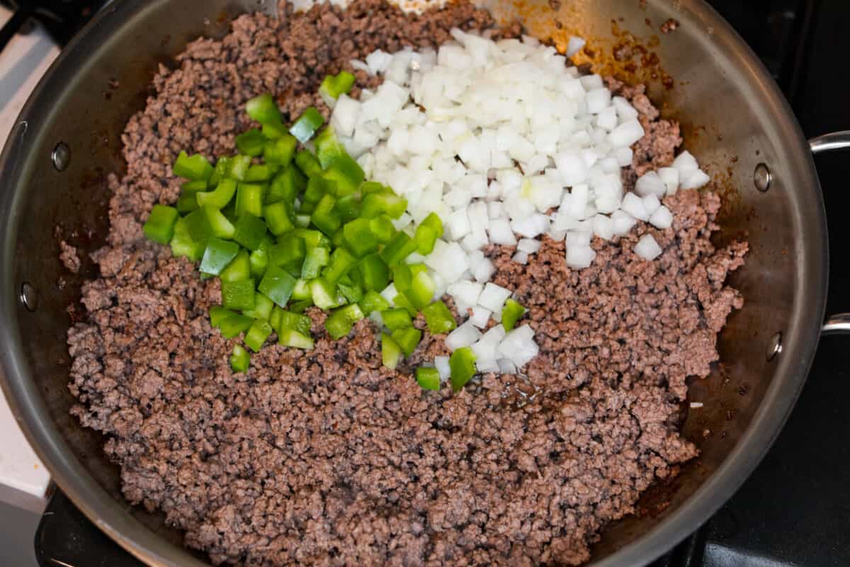 Cooked ground beef on the stove with onions and peppers being added. 