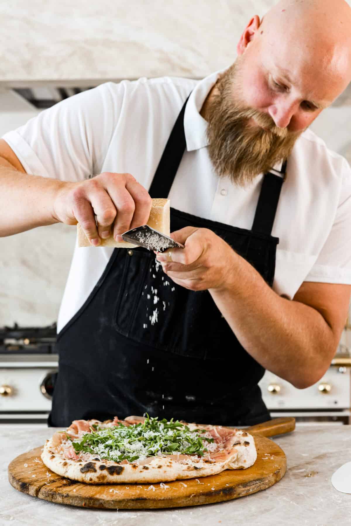 Close view of the chef grating parmesan cheese on the wood-fired pizza.