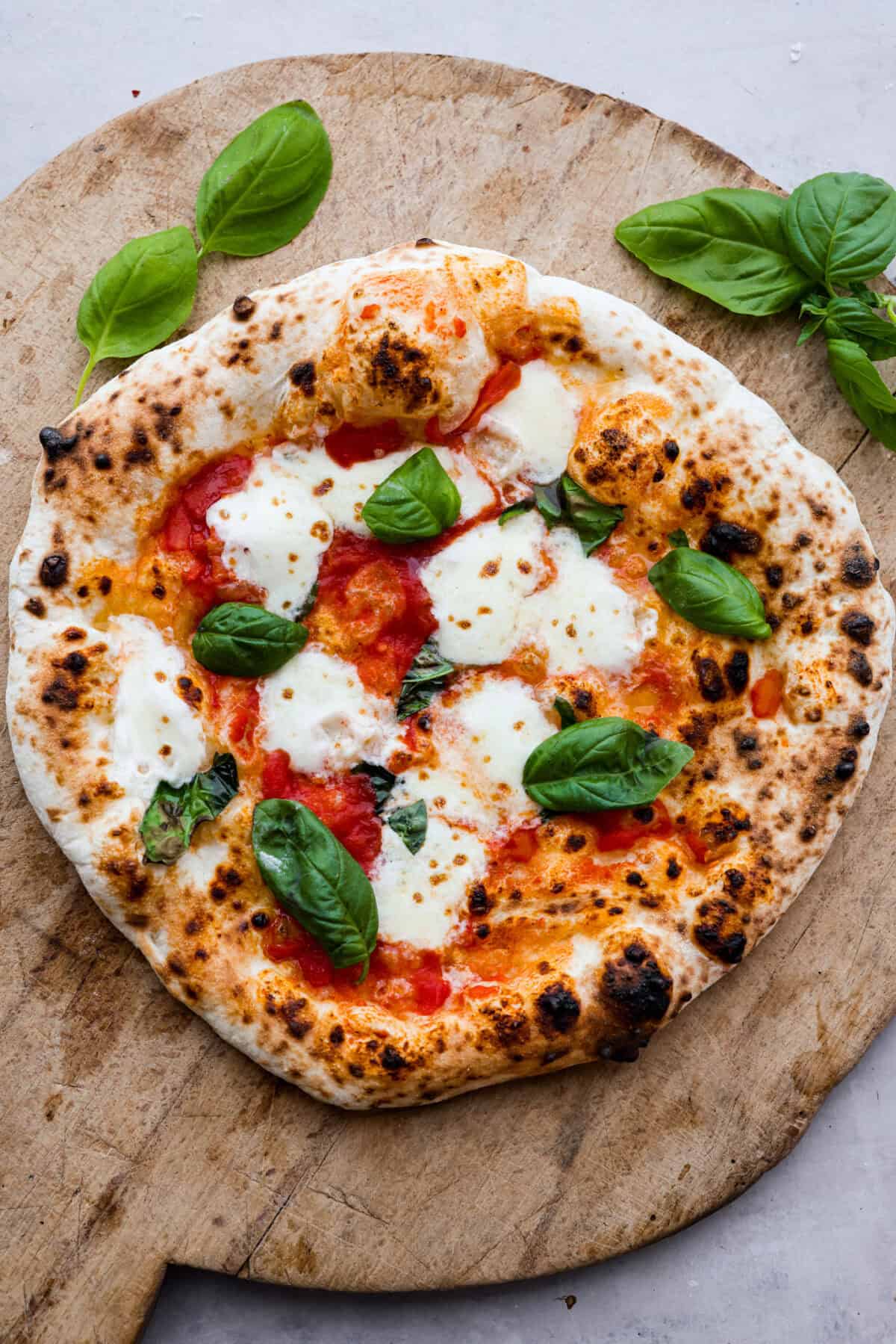 Top view of wood-fired pizza on a wood cutting board.