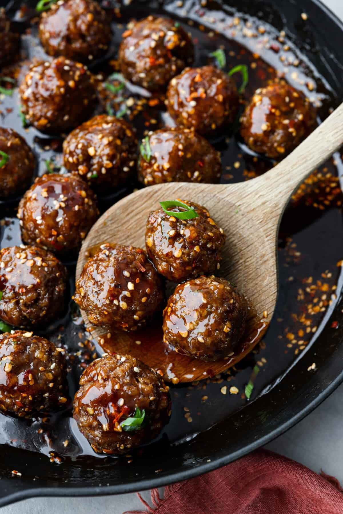 Close up shot of large wooden spoon scooping meatballs out of a skillet. 