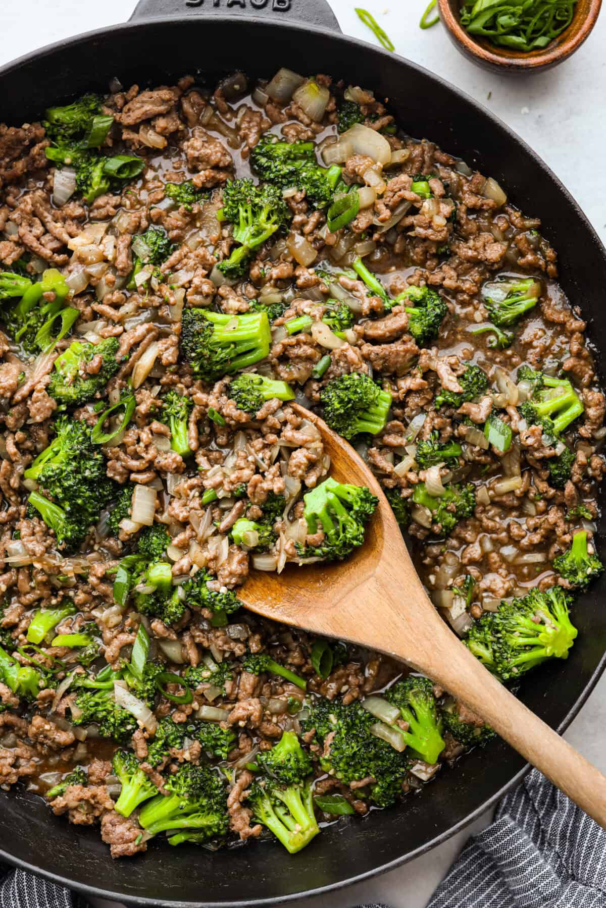 Overhead shot of ground beef and broccoli in skillet with wooden spoon. 