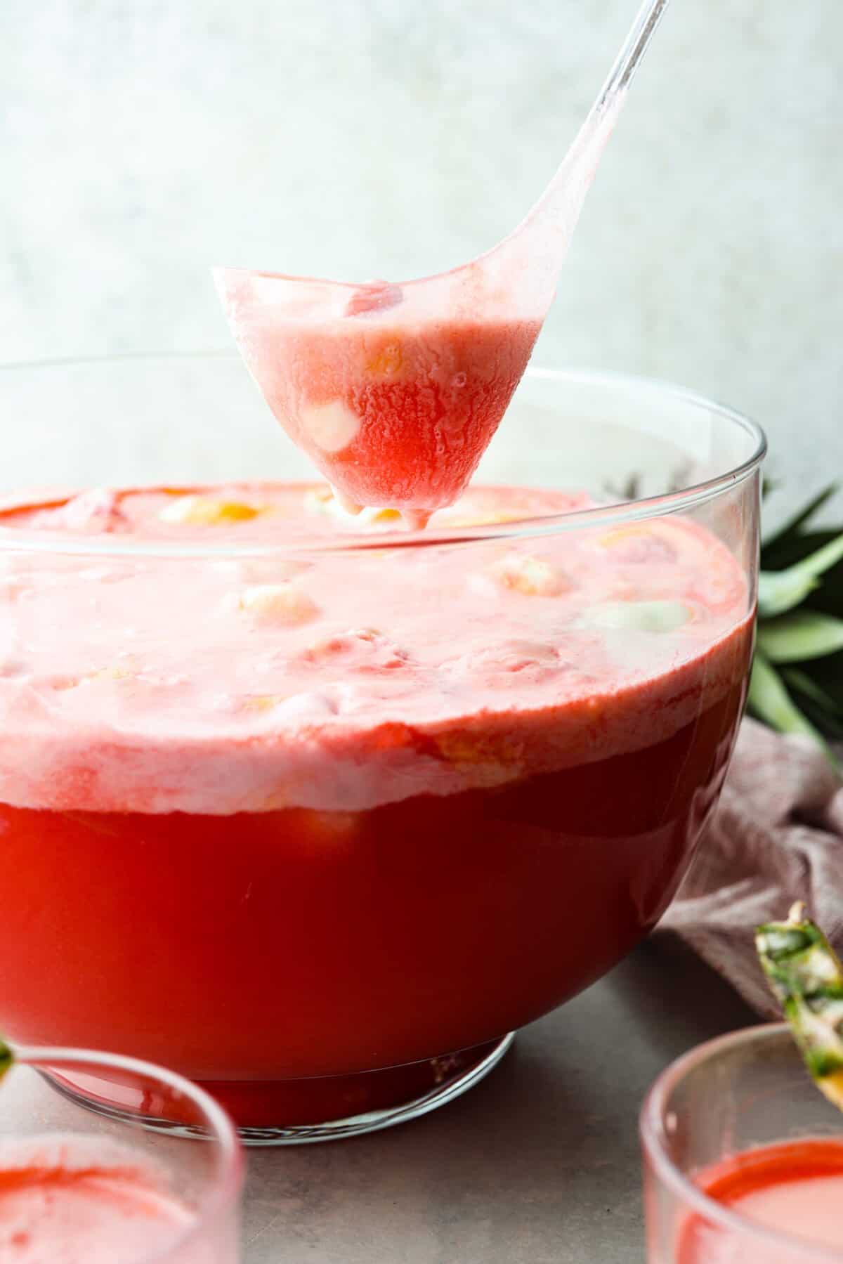 Side view of a large bowl filled with bright red punch that is topped with rainbow sherbet that has foam and big chunks of the sherbet.