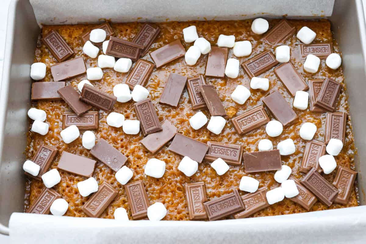 Overhead shot of of the pan with graham cracker layer with butter and sugar mixture topped with pieces of chocolate and mini marshmallows. 