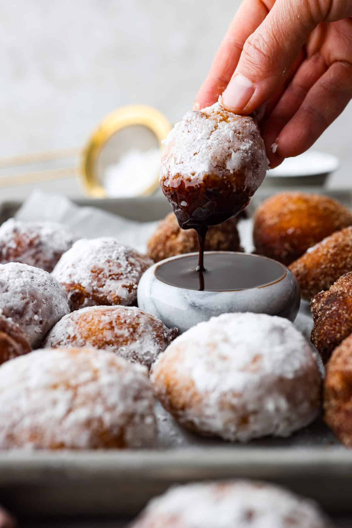 Side shot of someone dipping a zeppole in to chocolate sauce. 