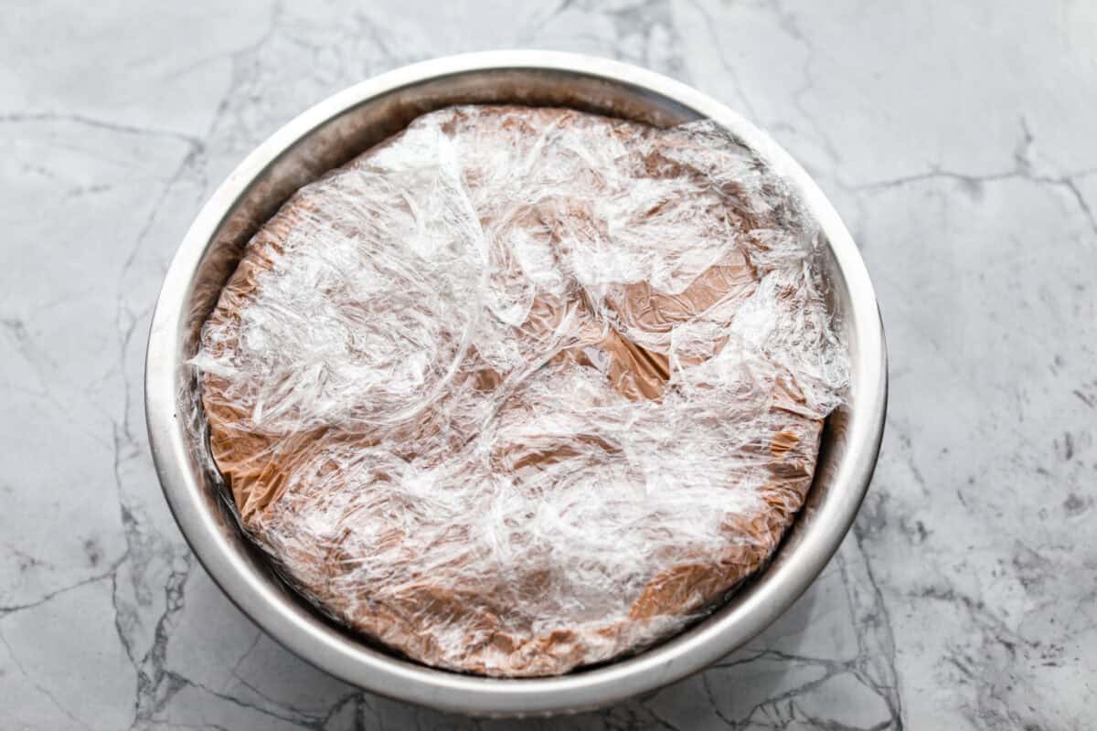 Overhead shot of large bowl with ice cream layers and plastic wrap covering the top. 