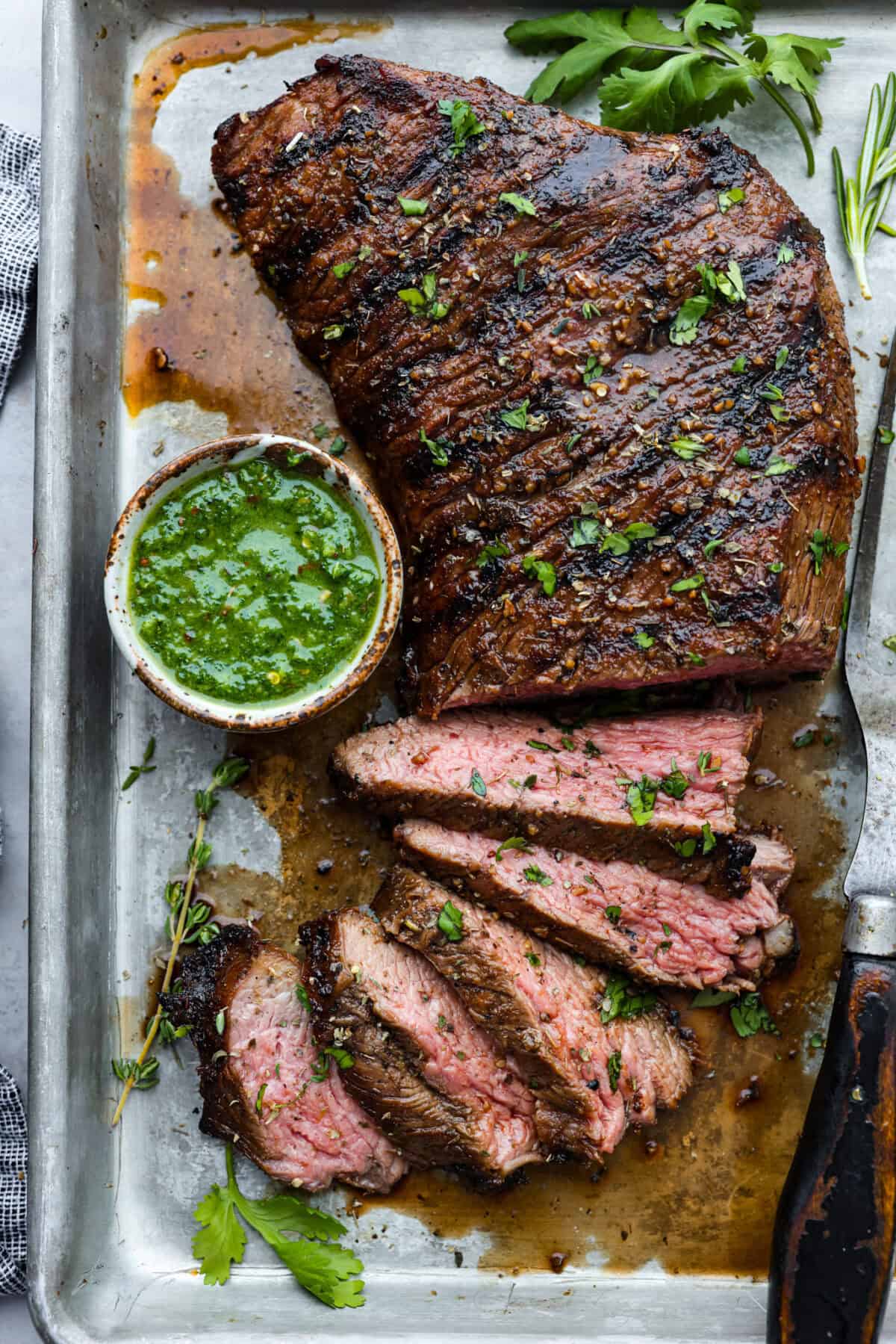 Overhead shot of grilled tri-tip that has a few slices taken off and a small bowl of chimichuri sauce next to it. 