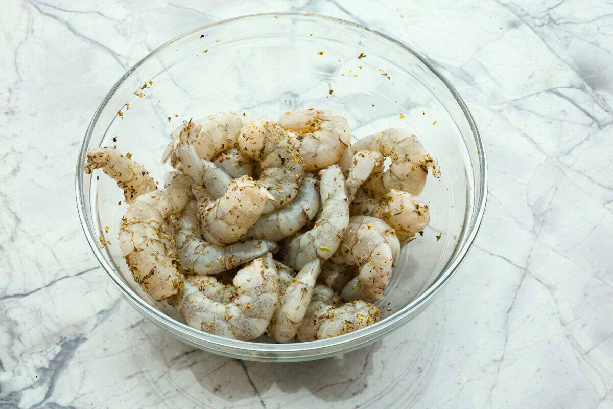 Overhead shot of a bowl of raw seasoned shrimp. 