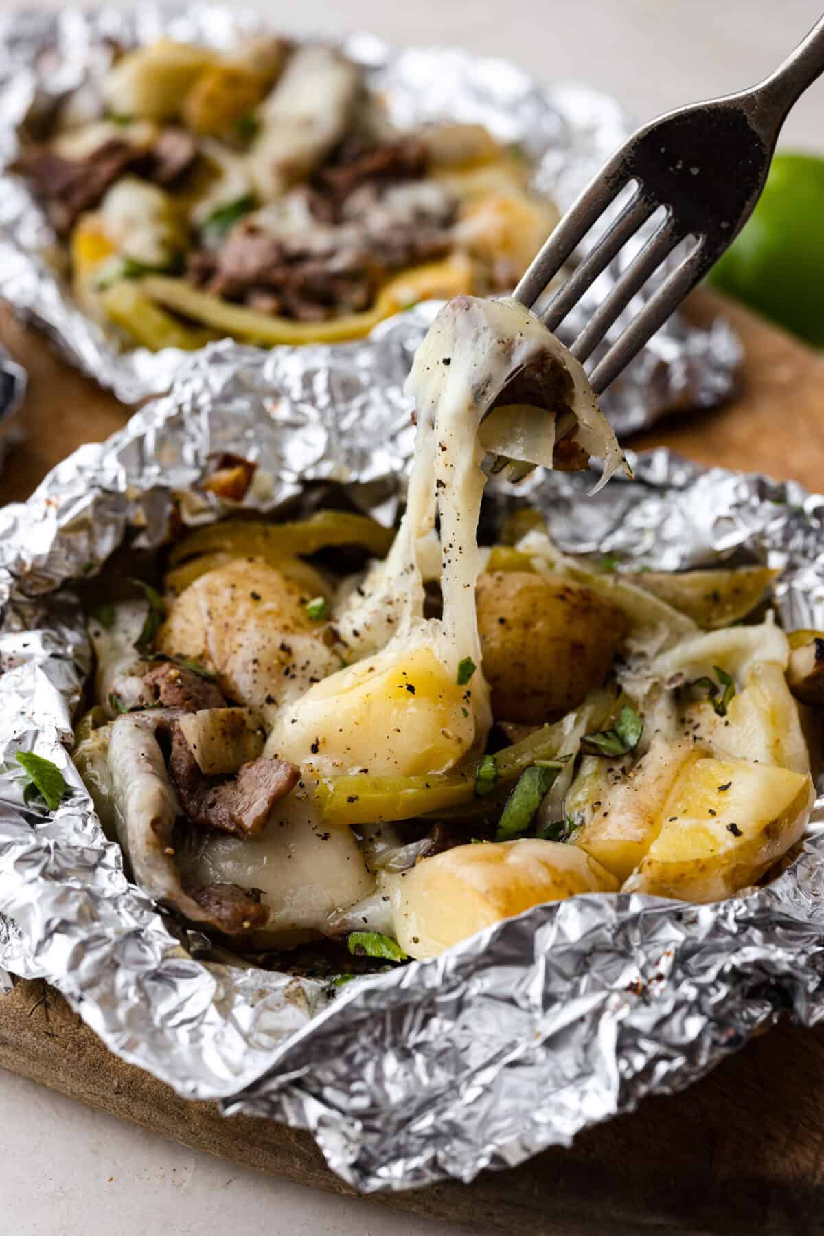 Close up shot of a fork lifting a bit of the cooked cheesesteak mixture with melty cheese stretching. 