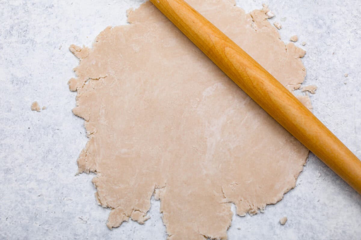 Overhead shot of pie crust being rolled out on floured surface, with rolling pin. 