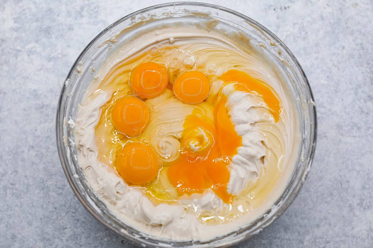 Overhead shot of eggs and vanilla added to cream cheese and sugar mixture in glass bowl. 