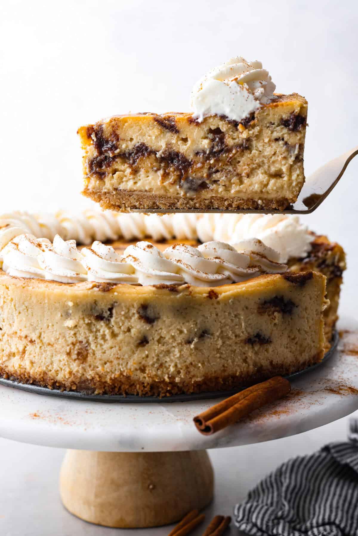 Side shot of slice of cheesecake being lifted out of the whole cinnamon roll cheesecake. 