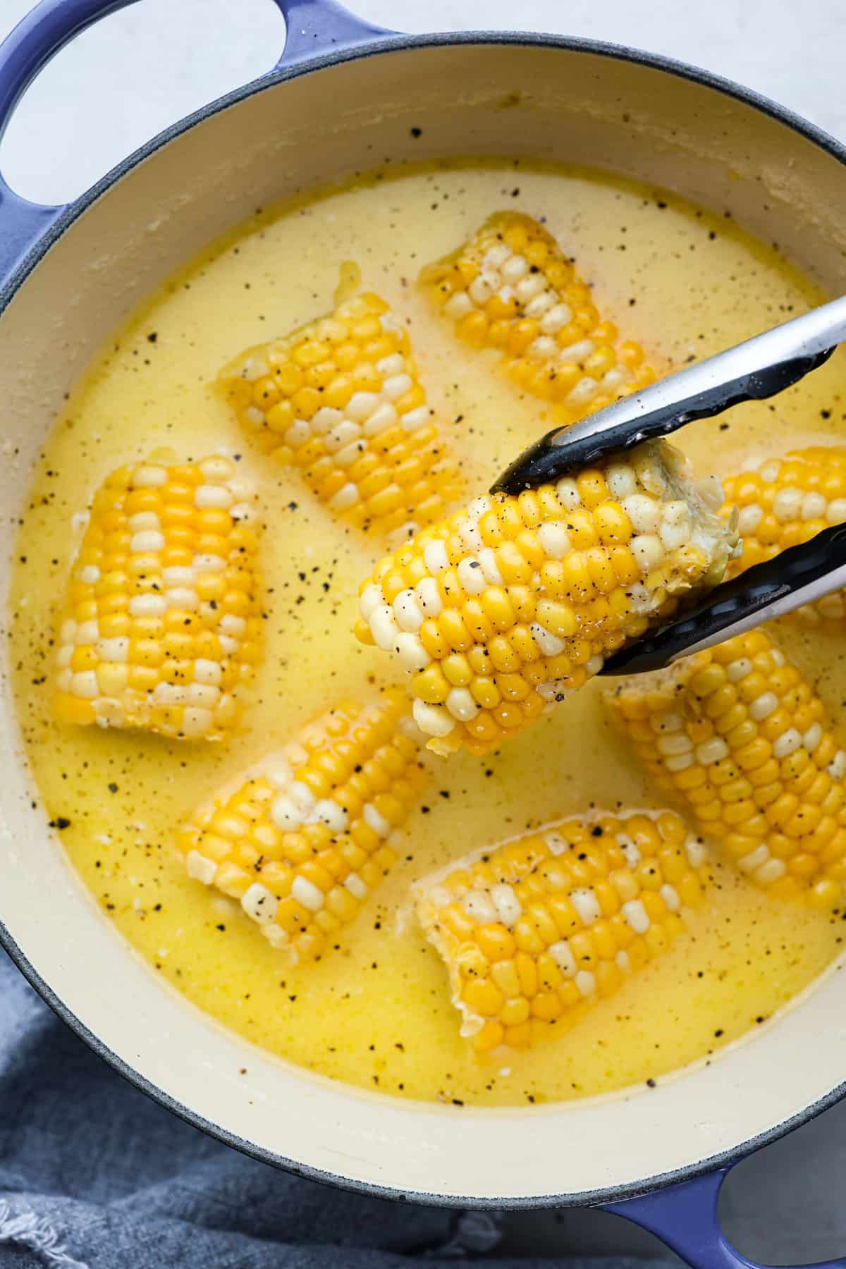 Close top view of tongs lifting up corn from a pot.