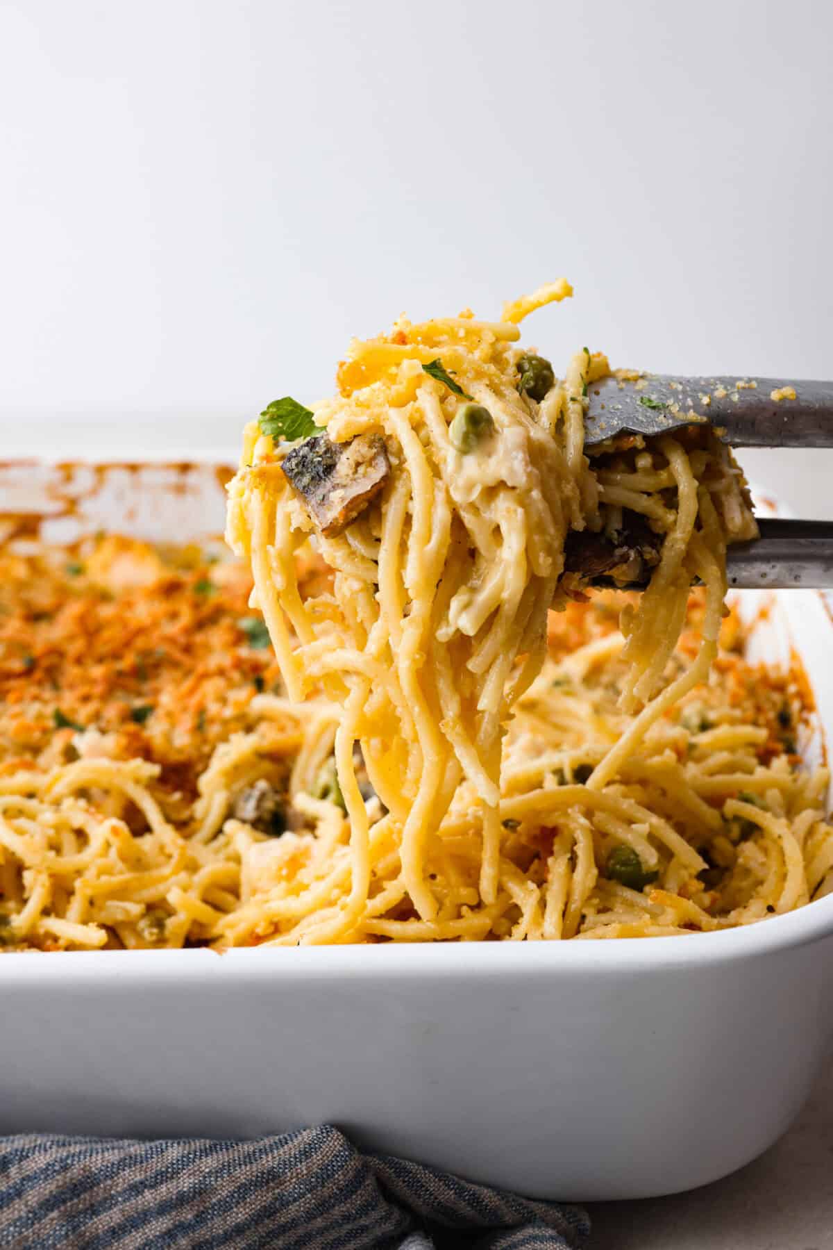 Side shot of tongs lifting a portion of chicken tetrazzini casserole out of the casserole dish. 