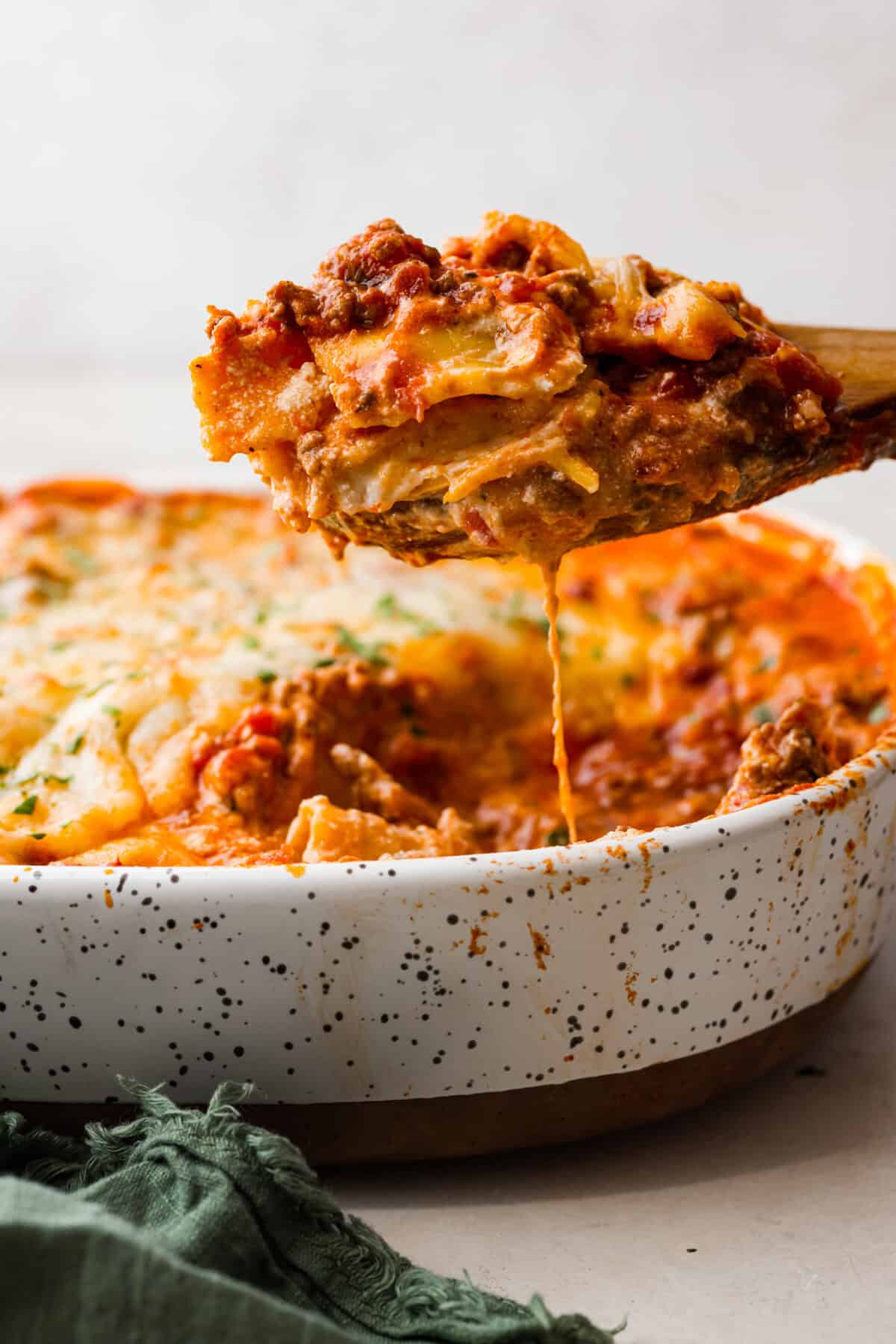 Side shot of a portion of million dollar ravioli casserole being scooped out of the baking dish. 