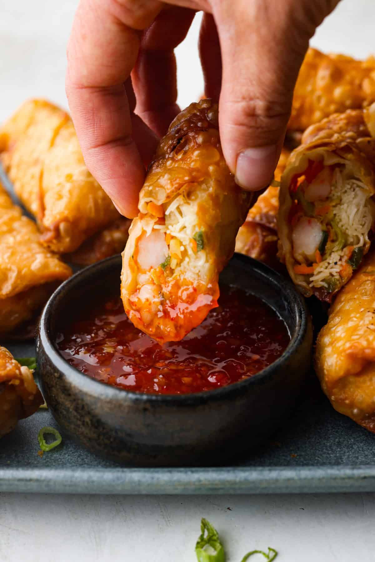 Close up shot of someone dipping a shrimp egg roll in sauce. 