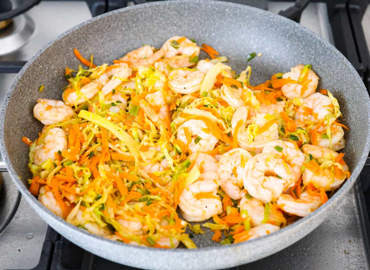 Overhead shot of shrimp and seasonings and sauces mixed in with the vegetables in a skillet. 