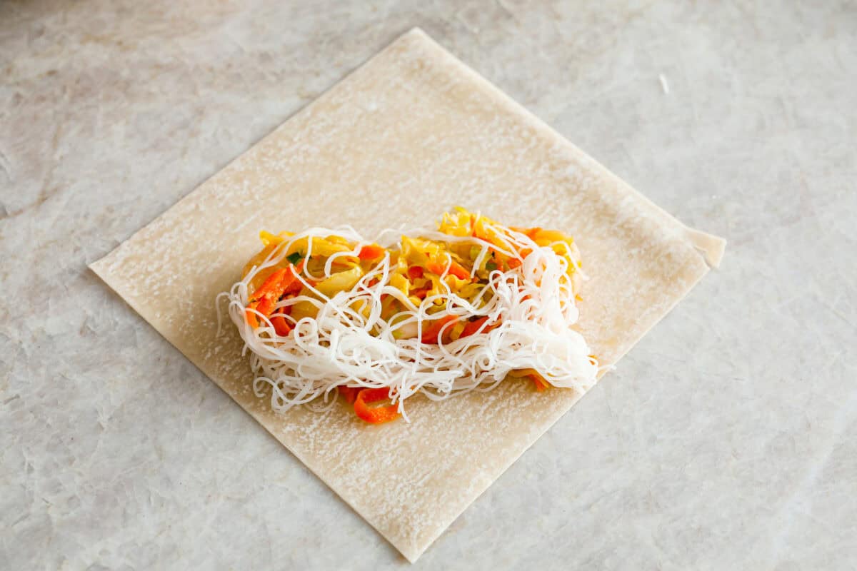 Overhead shot of noodles and veggie filling on an egg roll wrapper. 