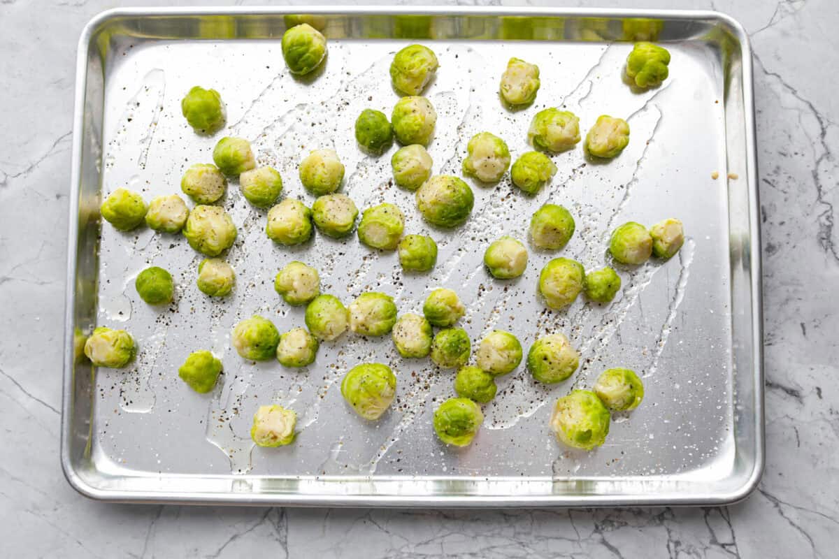Irresistibly crispy Smashed Brussels Sprouts are simple to make, loaded with delicious flavor, and have the best crunchy texture. These pair well with almost any protein and will definitely upgrade your side dish game! Overhead shot of boiled Brussels sprouts on a baking sheet drizzled with oil and sprinkled with salt and pepper.