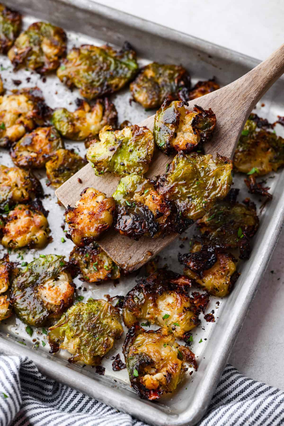 Irresistibly crispy Smashed Brussels Sprouts are simple to make, loaded with delicious flavor, and have the best crunchy texture. These pair well with almost any protein and will definitely upgrade your side dish game! Angle shot of a wooden spatula holding up a few smashed Brussels sprouts out of the pan.