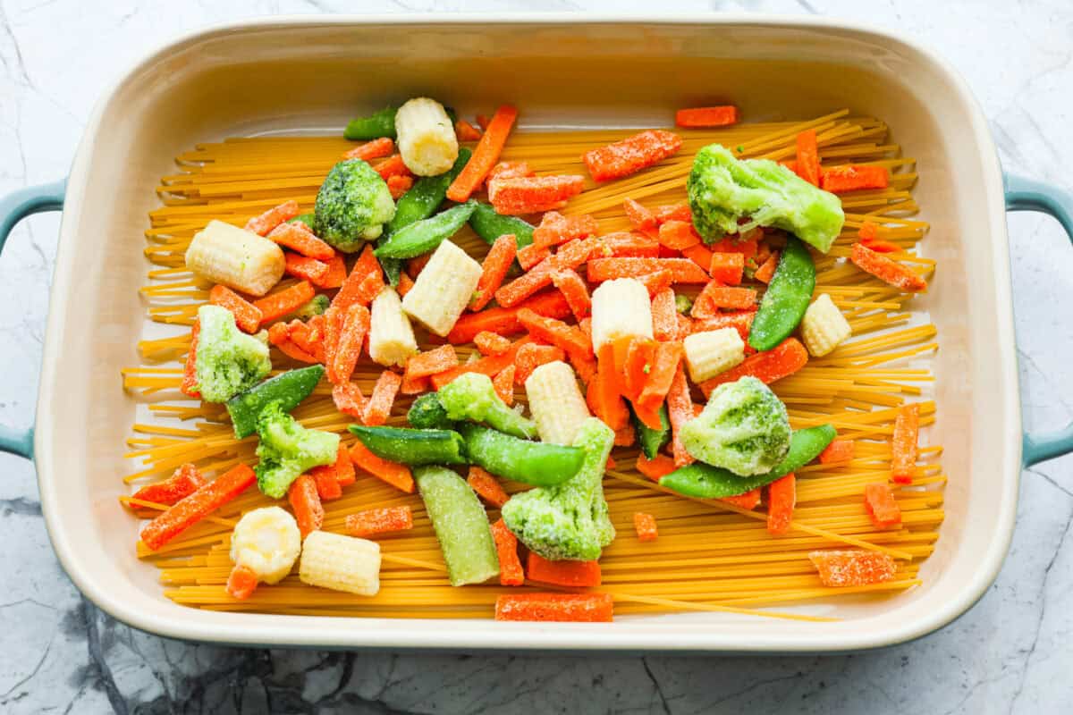 Overhead shot of frozen vegetables over noodles in a baking dish. 