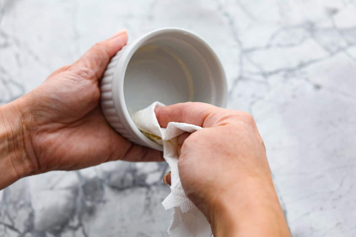 Overhead shot of someone prepping a ramekin with butter.