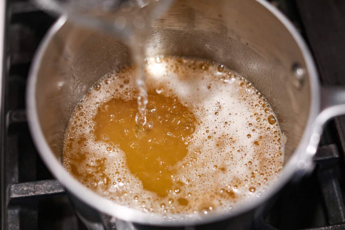 Overhead shot of someone pouring water into the browned butter. 