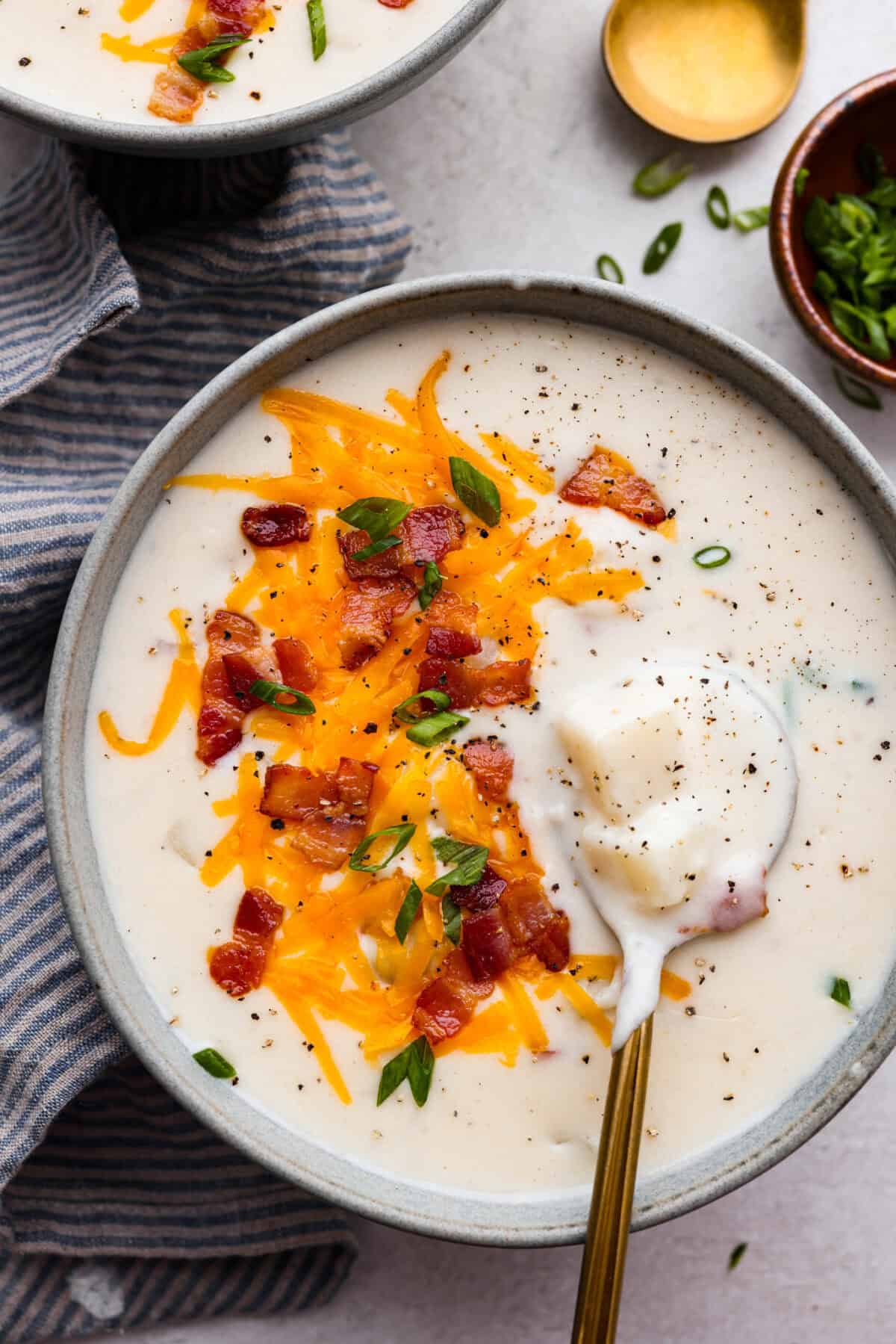 Overhead shot of a bowl of creamy potato soup with cheese, chives and bacon on top. 