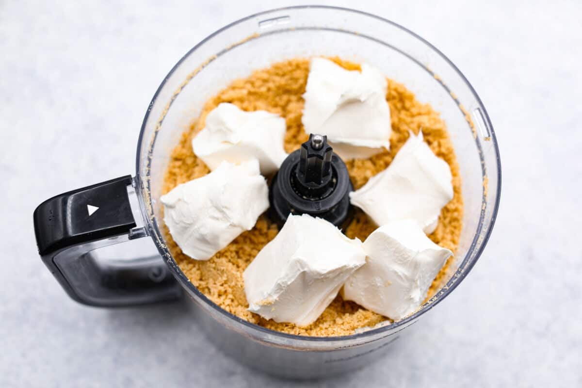 Overhead shot of Oreo cookie crumbs with chunks of cream cheese in a food processor. 