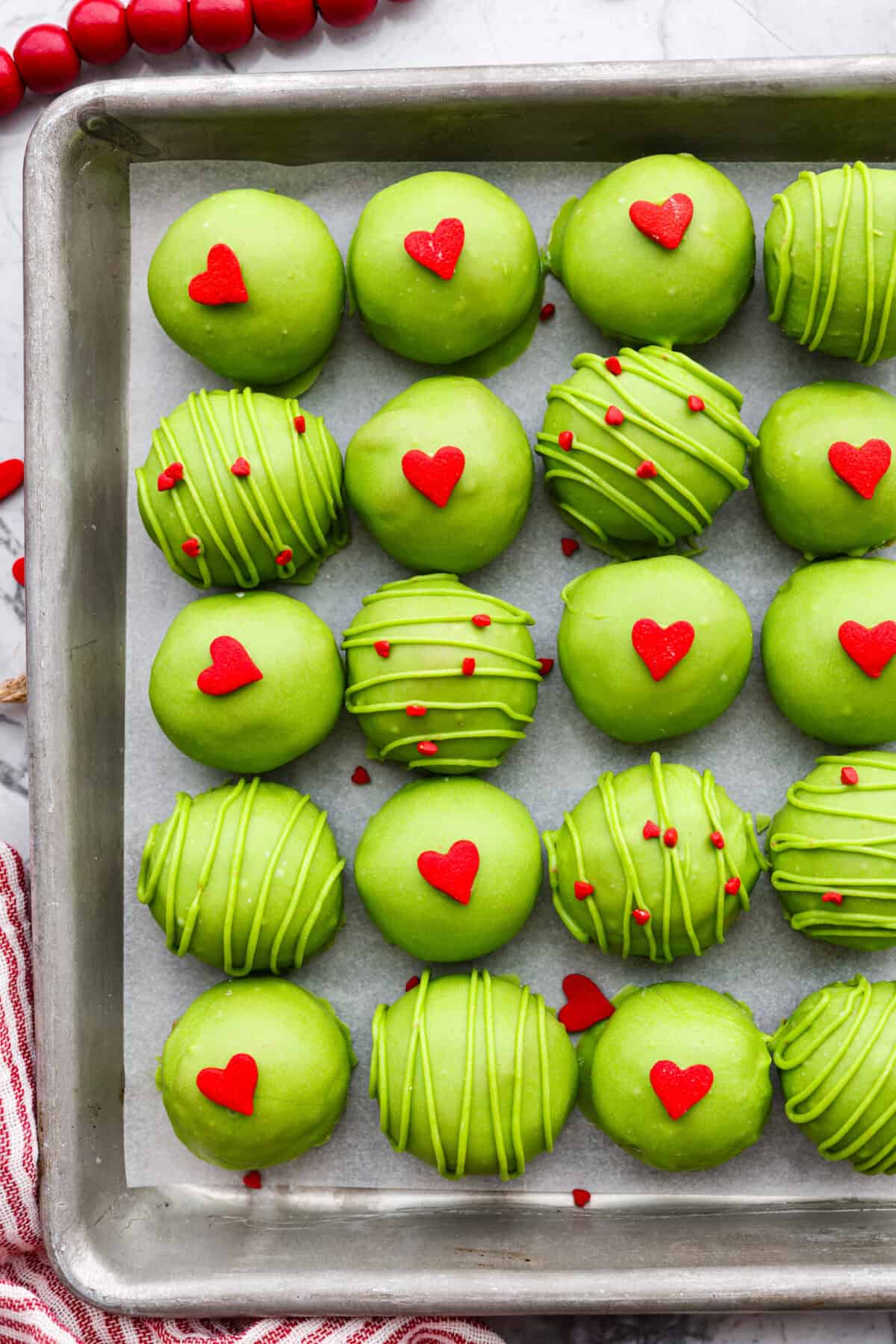 Overhead shot of a cookie sheet full of completed Grinch Oreo balls with red heart sprinkles. 