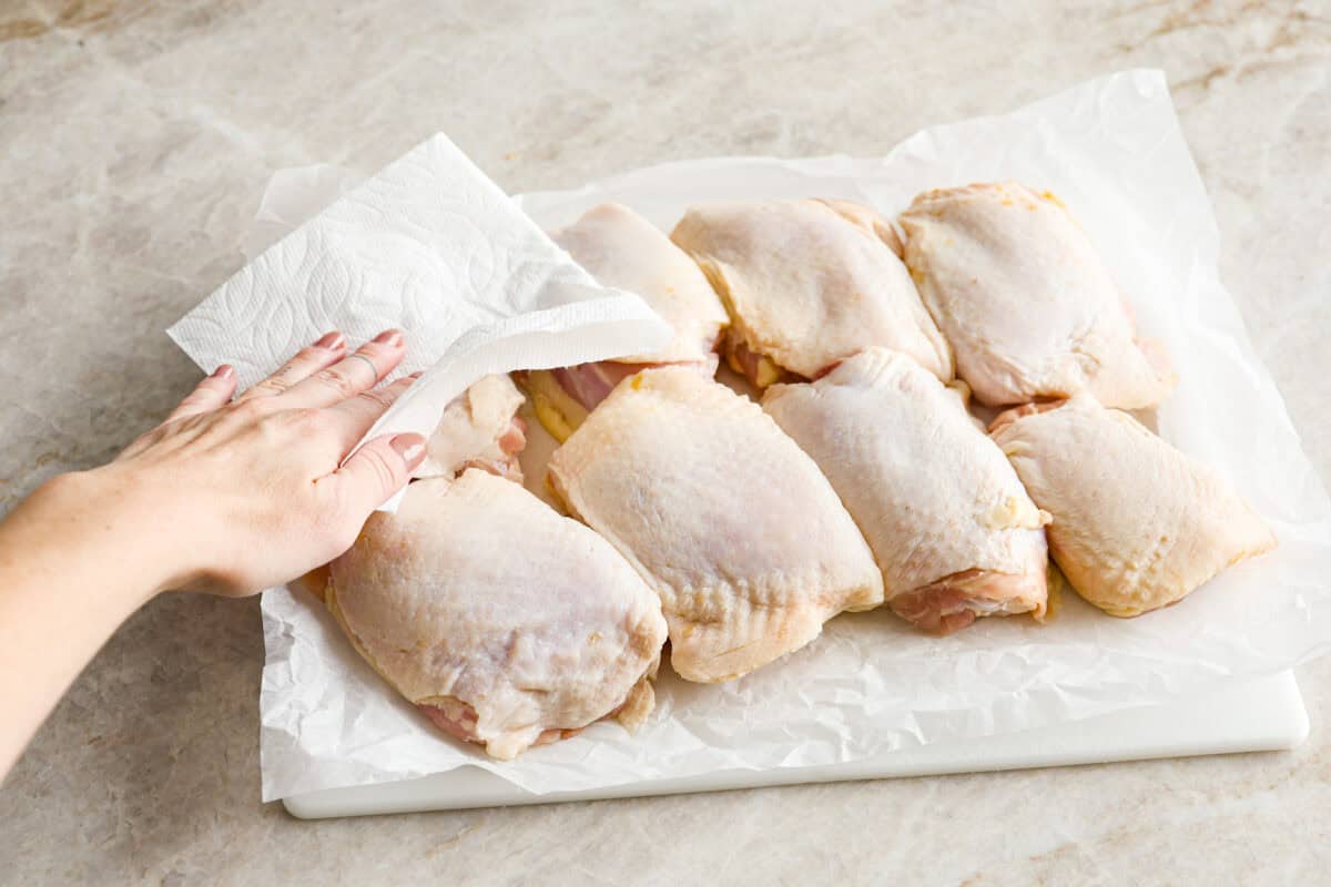 Angle shot of someone drying off the chicken thighs with a paper towel.