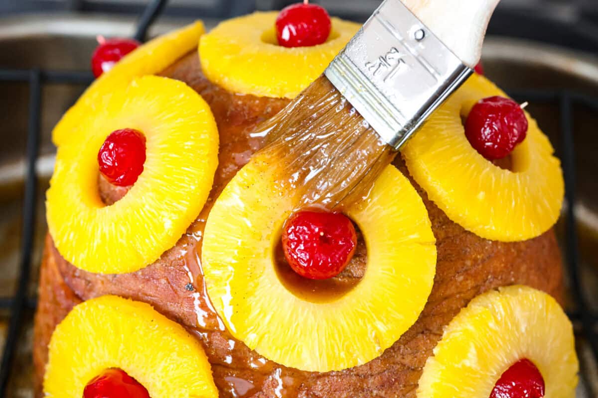 Close up shot of someone putting a second coat of the pineapple glaze on the ham.