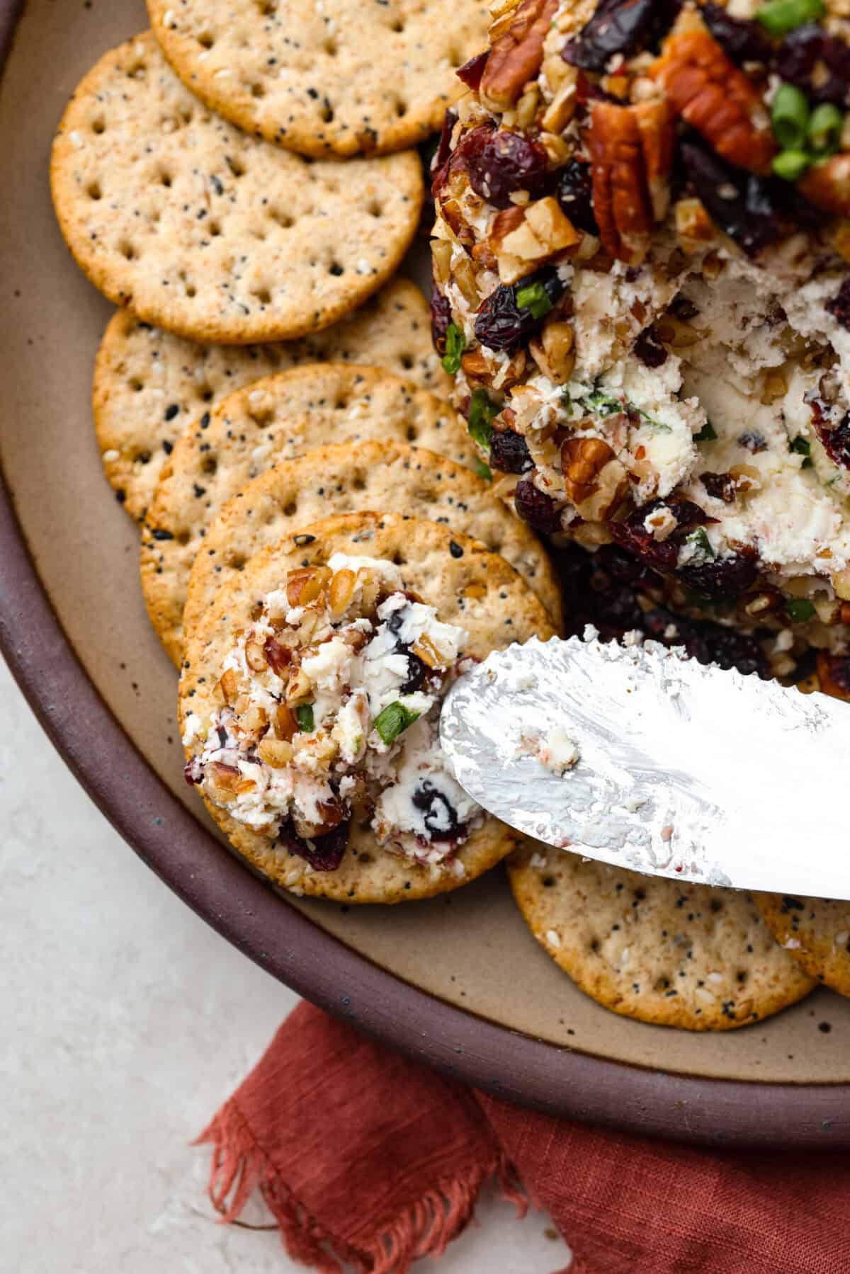 Top close view of a knife spreading cheese ball on a cracker.