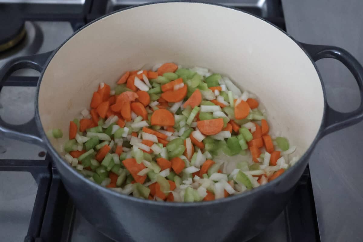 This creamy chicken noodle soup tastes exactly how it sounds! It's classic chicken noodle soup but creamy, rich and filling! Loaded with hearty chicken, tender carrots, supple noodles, and lots of delicious flavors, it's perfect for winter! Angle shot of carrots, celery and onions cooking in a pot on the stove.