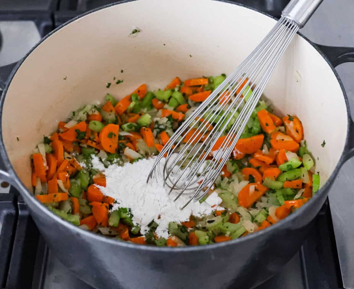 This creamy chicken noodle soup tastes exactly how it sounds! It's classic chicken noodle soup but creamy, rich and filling! Loaded with hearty chicken, tender carrots, supple noodles, and lots of delicious flavors, it's perfect for winter! Angle shot of cooked vegetables with butter and flour being whisked in.