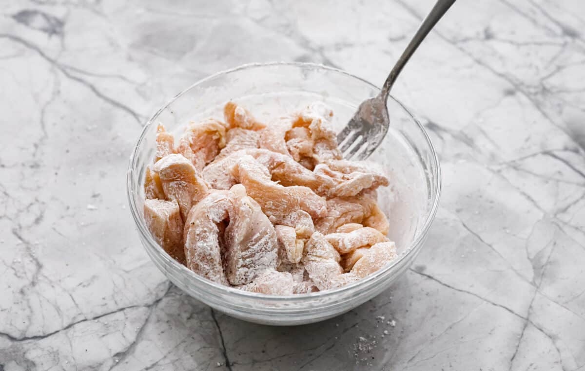 Hunan chicken is a tasty take-out favorite that can be made right at home! Tender chicken and veggies are tossed in the signature hunan sauce. It's savory with a hint of sweet and spicy! This easy one-pan dinner is ready in 30 minutes! First photo of the chicken coated with cornstarch.