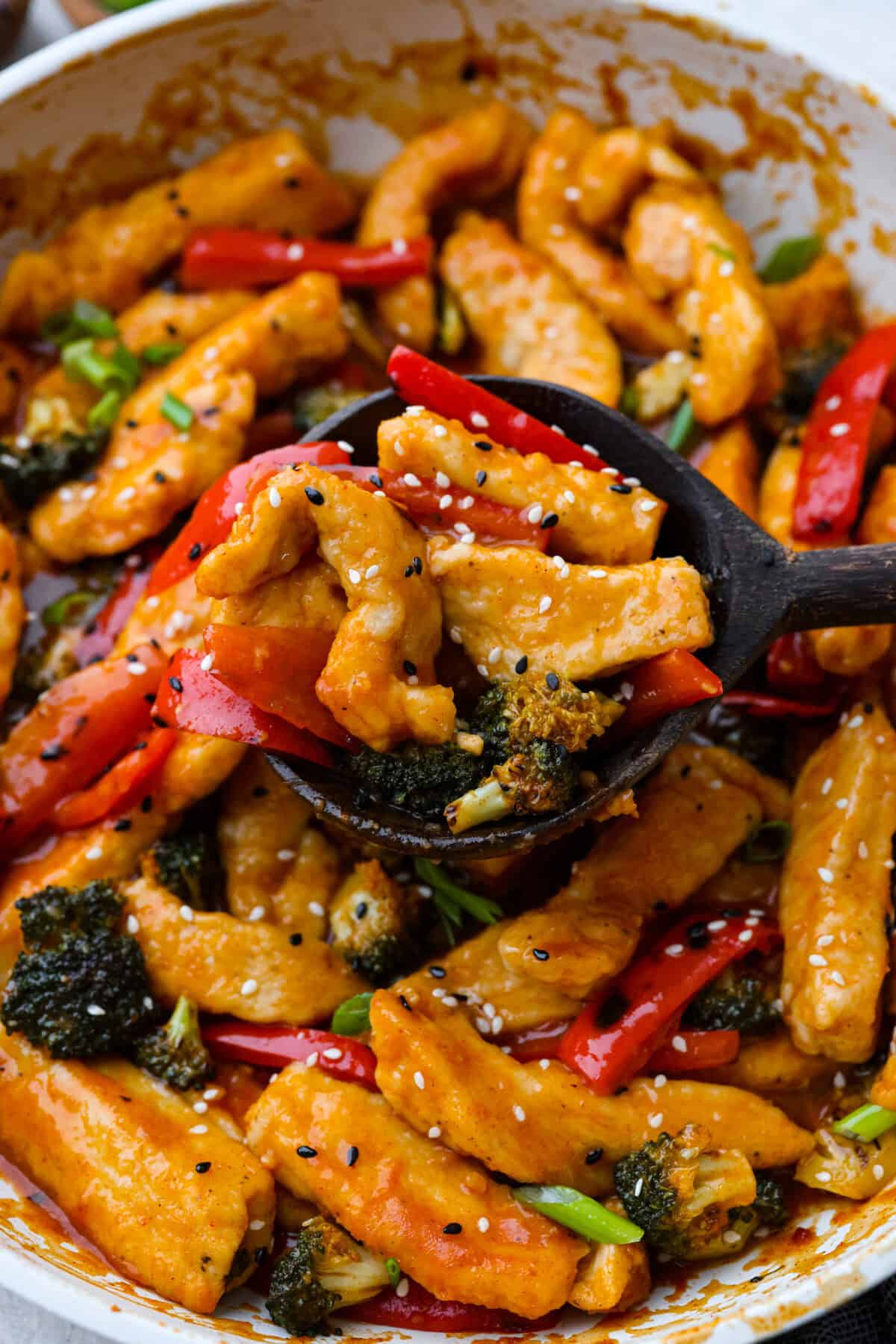 Hunan chicken is a tasty take-out favorite that can be made right at home! Tender chicken and veggies are tossed in the signature hunan sauce. It's savory with a hint of sweet and spicy! This easy one-pan dinner is ready in 30 minutes! Close view of Hunan chicken on a wooden serving spoon.