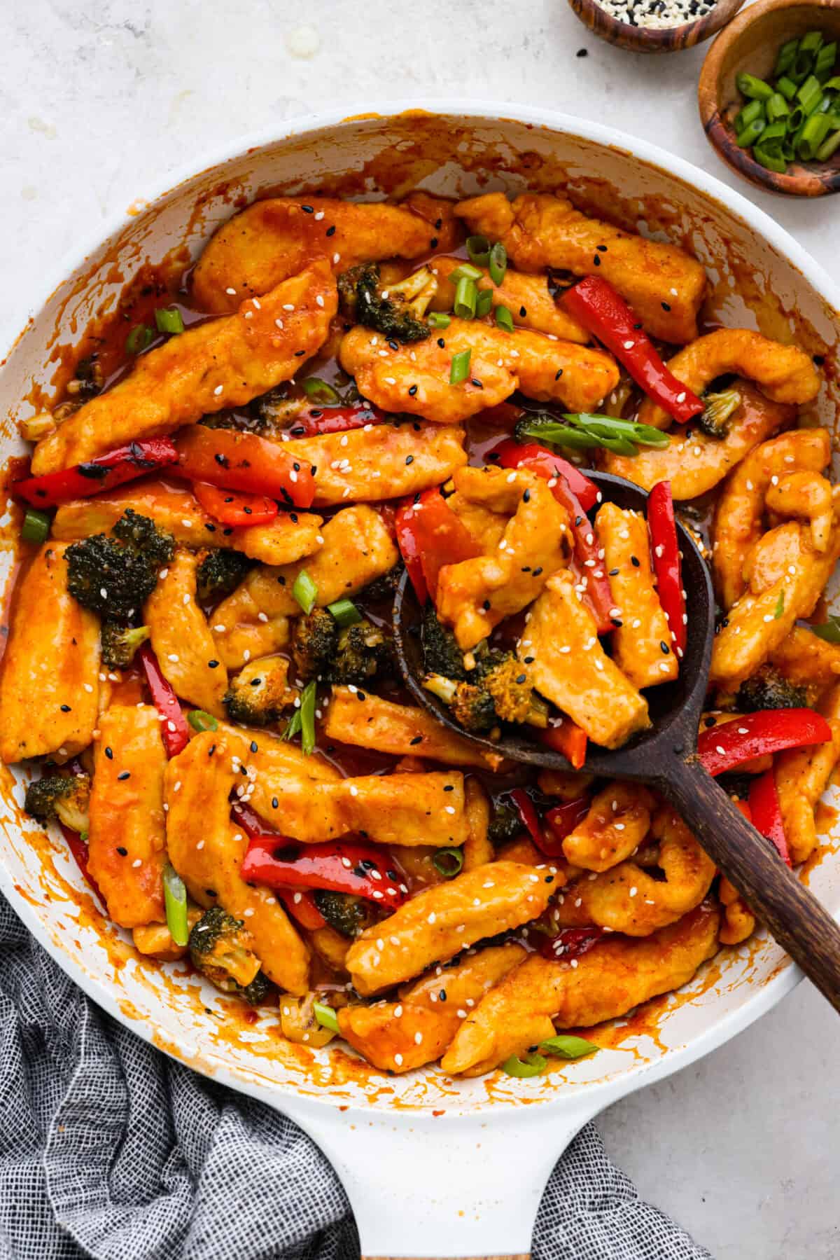 Hunan chicken is a tasty take-out favorite that can be made right at home! Tender chicken and veggies are tossed in the signature hunan sauce. It's savory with a hint of sweet and spicy! This easy one-pan dinner is ready in 30 minutes! Top view of Hunan chicken in a white skillet with a wood serving spoon.