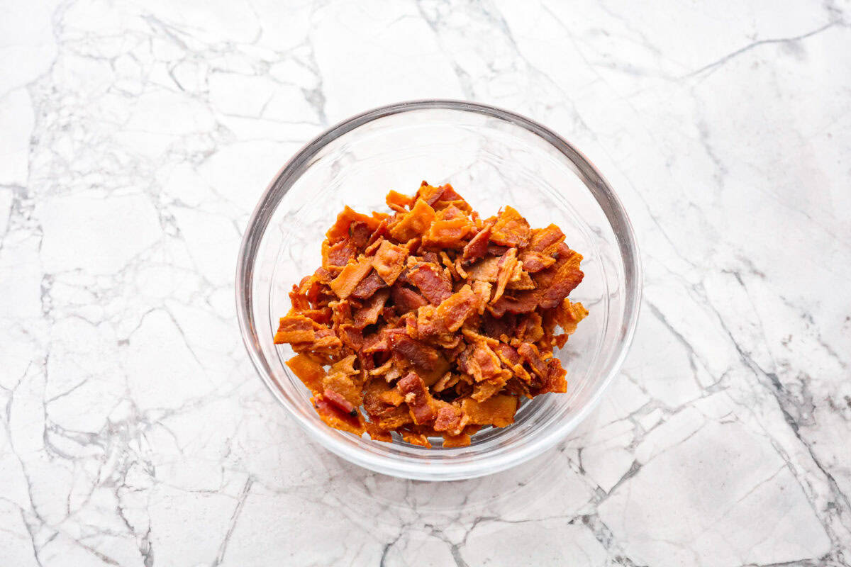 Maple Bacon Crack is as delicious and addicting as it sounds! It has flaky pastry dough drizzled in a sweet maple sauce and is loaded with crispy bacon pieces! It's the perfect sweet and salty snack! Overhead shot of a bowl of cooked bacon bits.